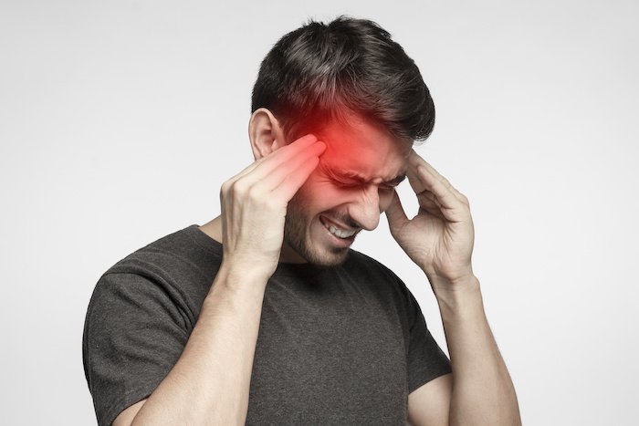 Closeup of young man touching temples with fingers as if suffering from severe migraine, feeling sick, isolated on gray background, simulating the heachache side effect of enclomiphene citrate